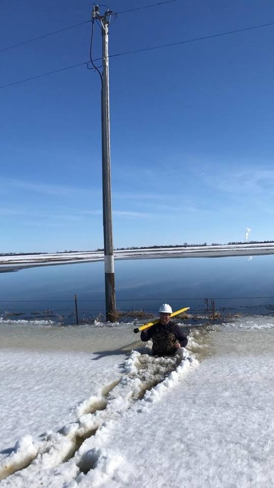 Lineman Jon Reichert wades into chest high ice and water in a ditch to make a repair on a pole.